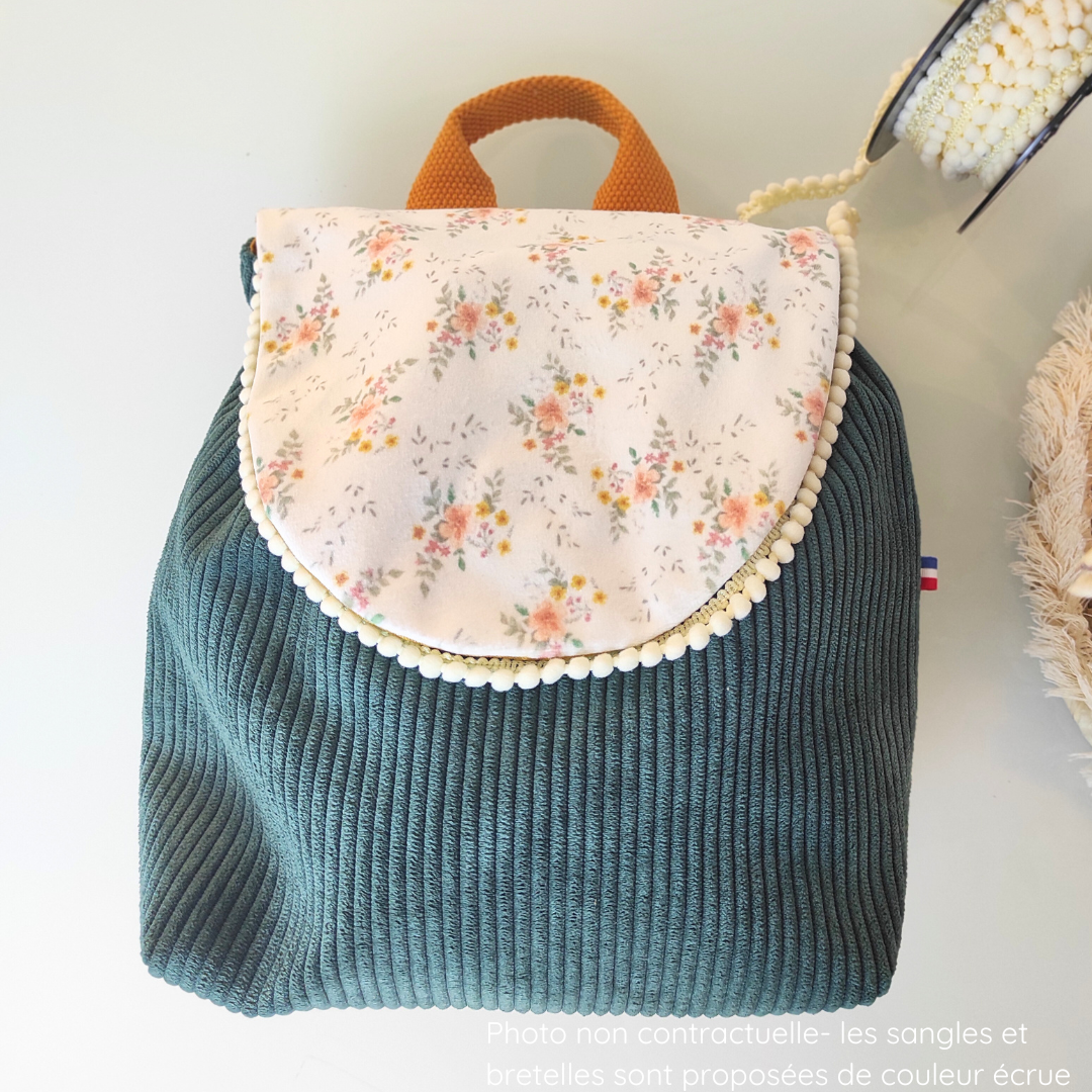 Un ruban avec pompons et placé sur le sac en velours vert canard.