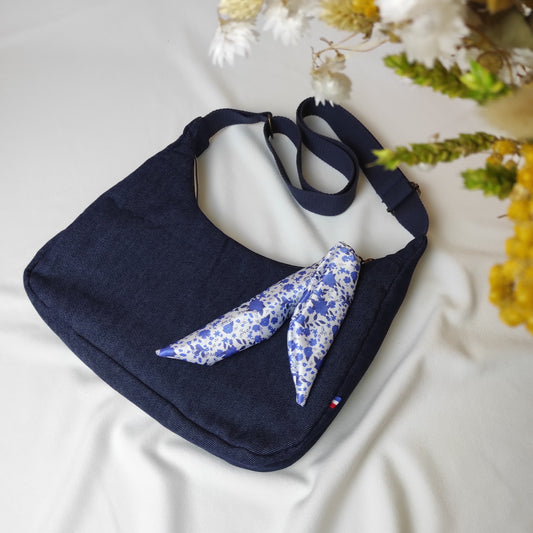 Sac besace en jean bleu marine avec ruban en satin fleuri, motif fleurs bleues avec fond blanc. La sangle est réglable.