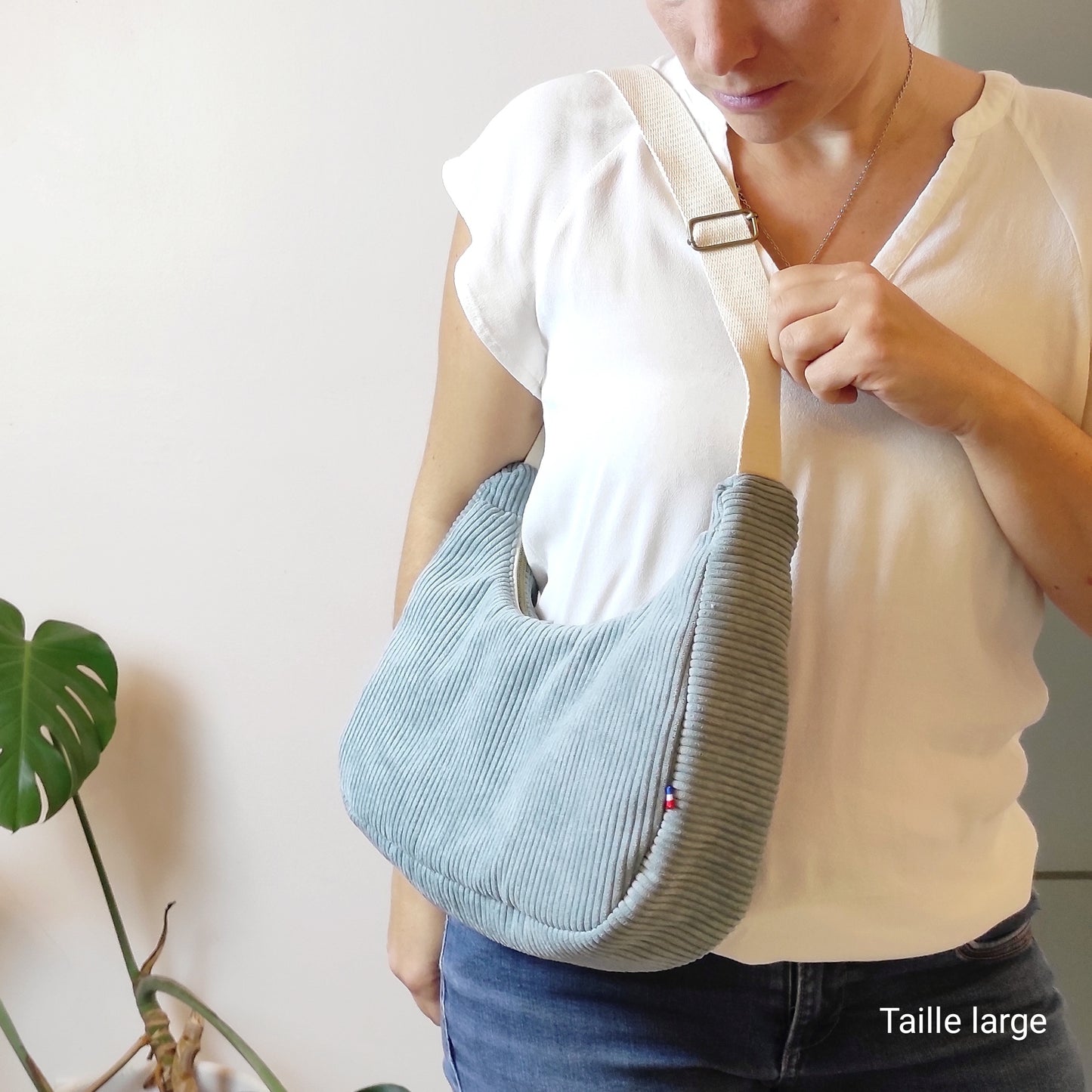 Sac en velours vert de gris, porté en sac à main sur l'épaule, sangle beige réglable.
