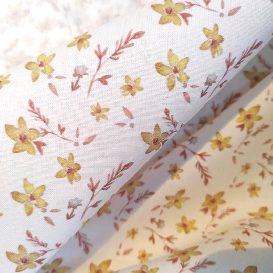 Tissu au motif exclusif fleurs dorées dessinées à l' aquarelle par Fanny Agustin. Les fleurs sont jaunes avec du feuillage marron sur fond blanc, le motif est doux et délicat.