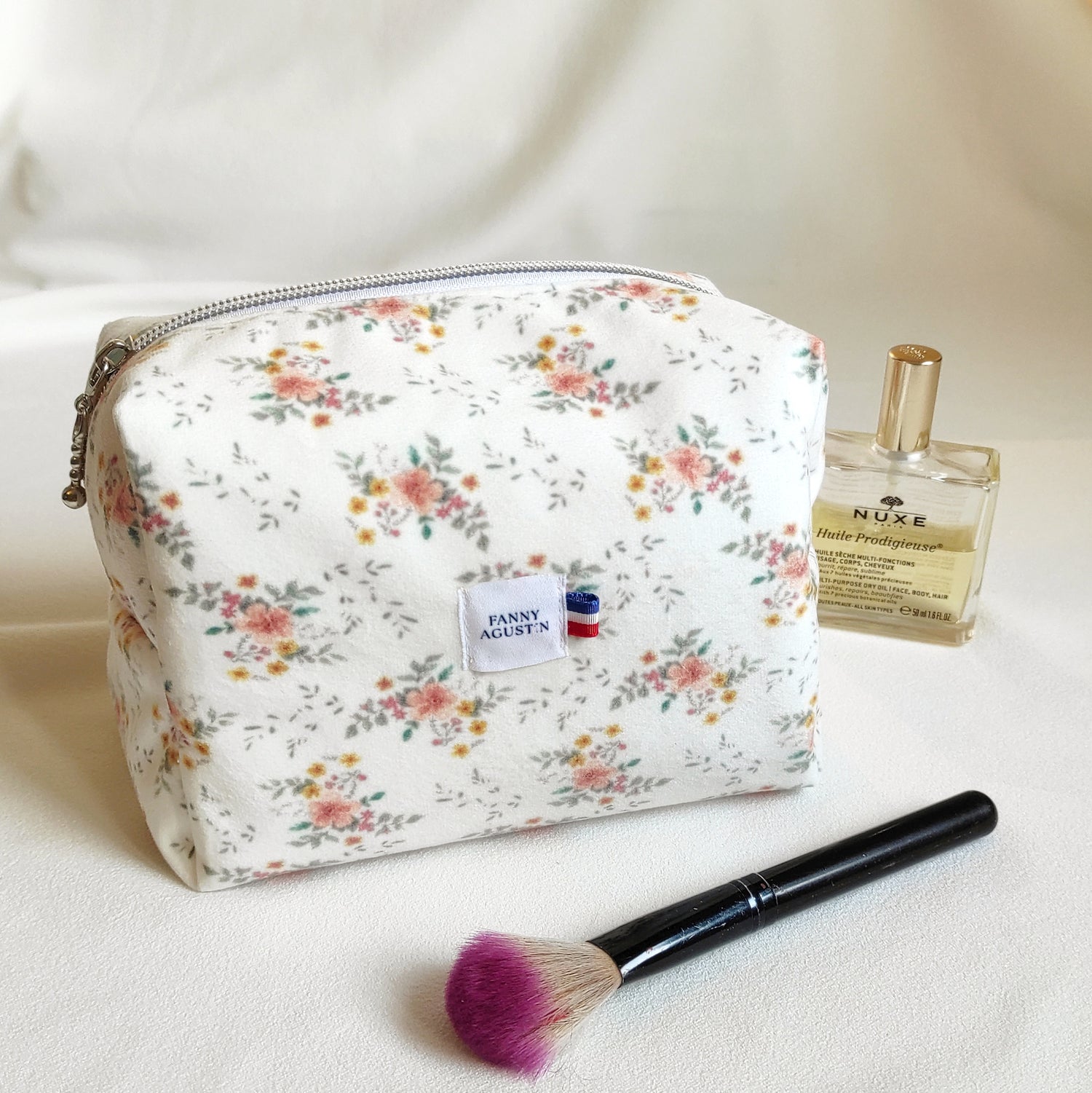 Trousse de toilette en velours doux imprimé localement et fabrication Française. Le dessin des fleurs est réalisé par Fanny Agustin ainsi que la fabrication à la main. 
La trousse en photographie est de taille normale, on peut y ajouter des accessoires à maquillage ou parfum comme représenté sur la photographie. Les motifs sont doux, avec du jaune, saumon et vert sur fond blanc.