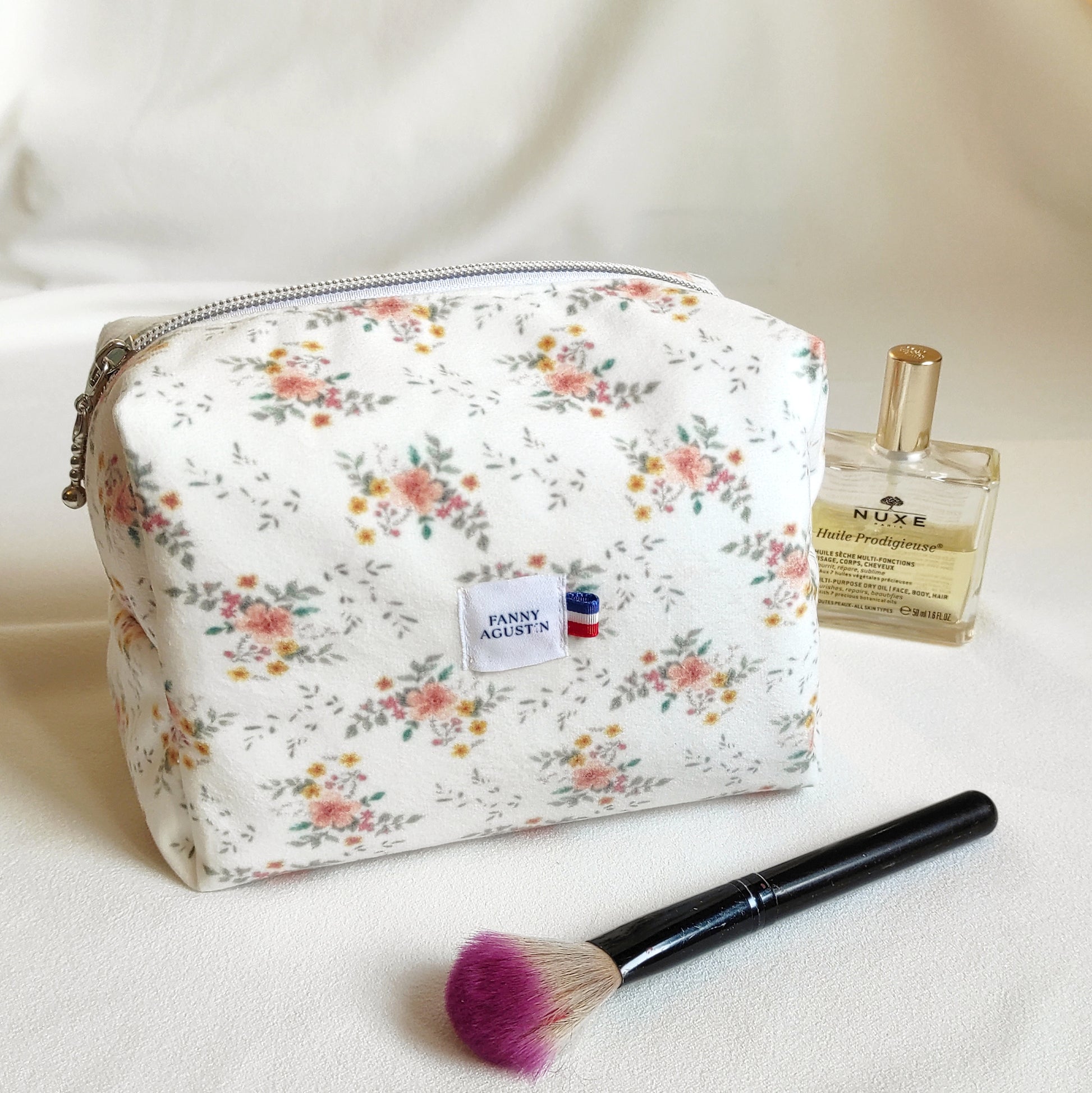 Trousse de toilette en velours doux imprimé localement et fabrication Française. Le dessin des fleurs est réalisé par Fanny Agustin ainsi que la fabrication à la main. 
La trousse en photographie est de taille normale, on peut y ajouter des accessoires à maquillage ou parfum comme représenté sur la photographie. Les motifs sont doux, avec du jaune, saumon et vert sur fond blanc.