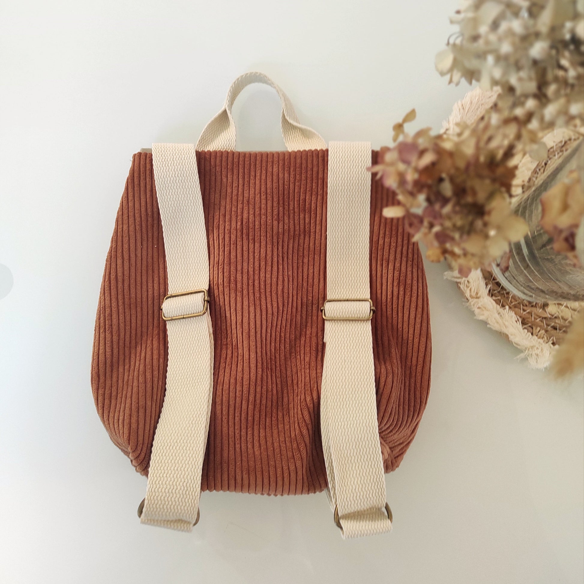 Sac à dos en velours vu de dos, avec bretelles en sangles écrues réglables.