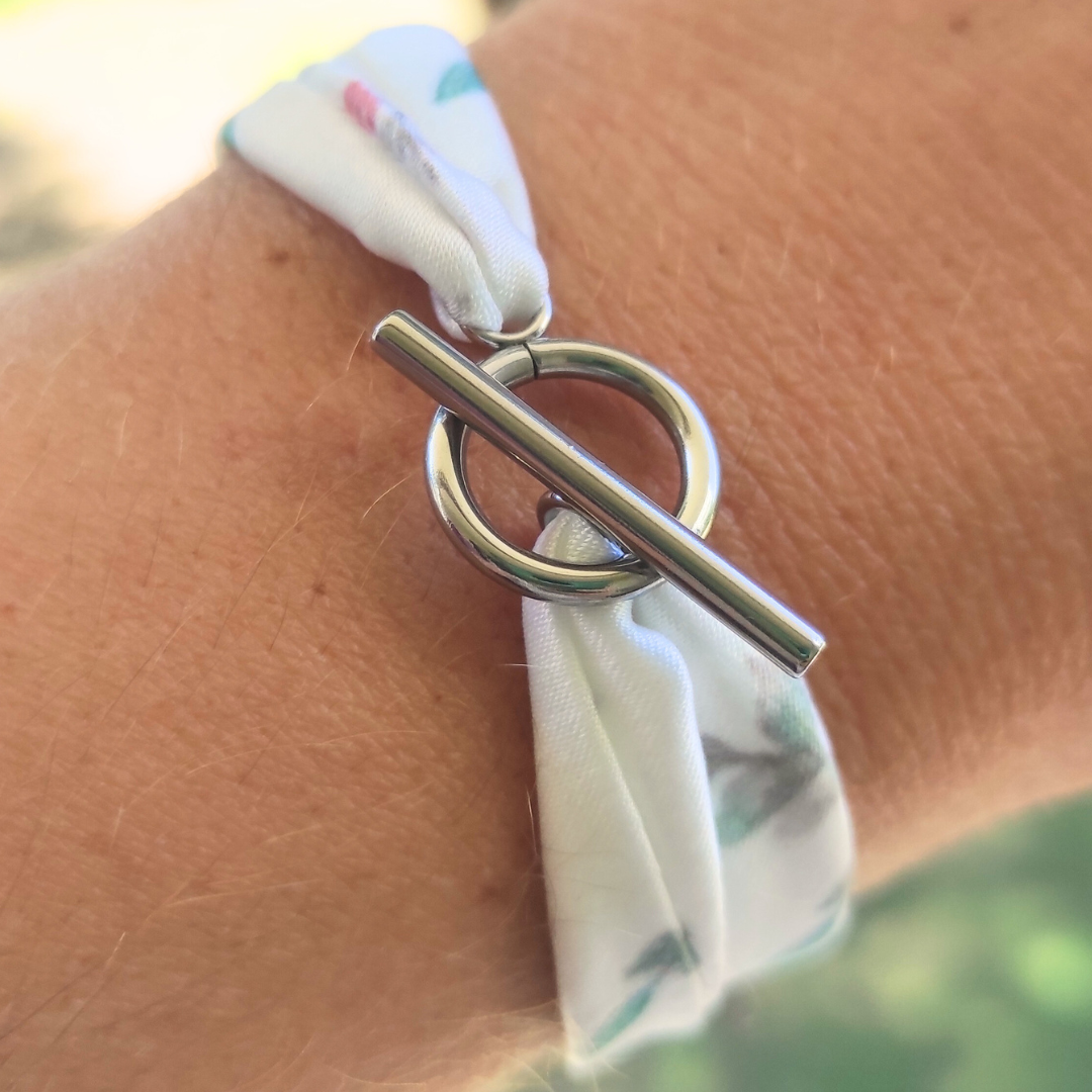 Bracelet en tissu satin motif feuillage, fond blanc avec quelques touches vertes et roses, avec fermoir anneau en acier inoxydable.