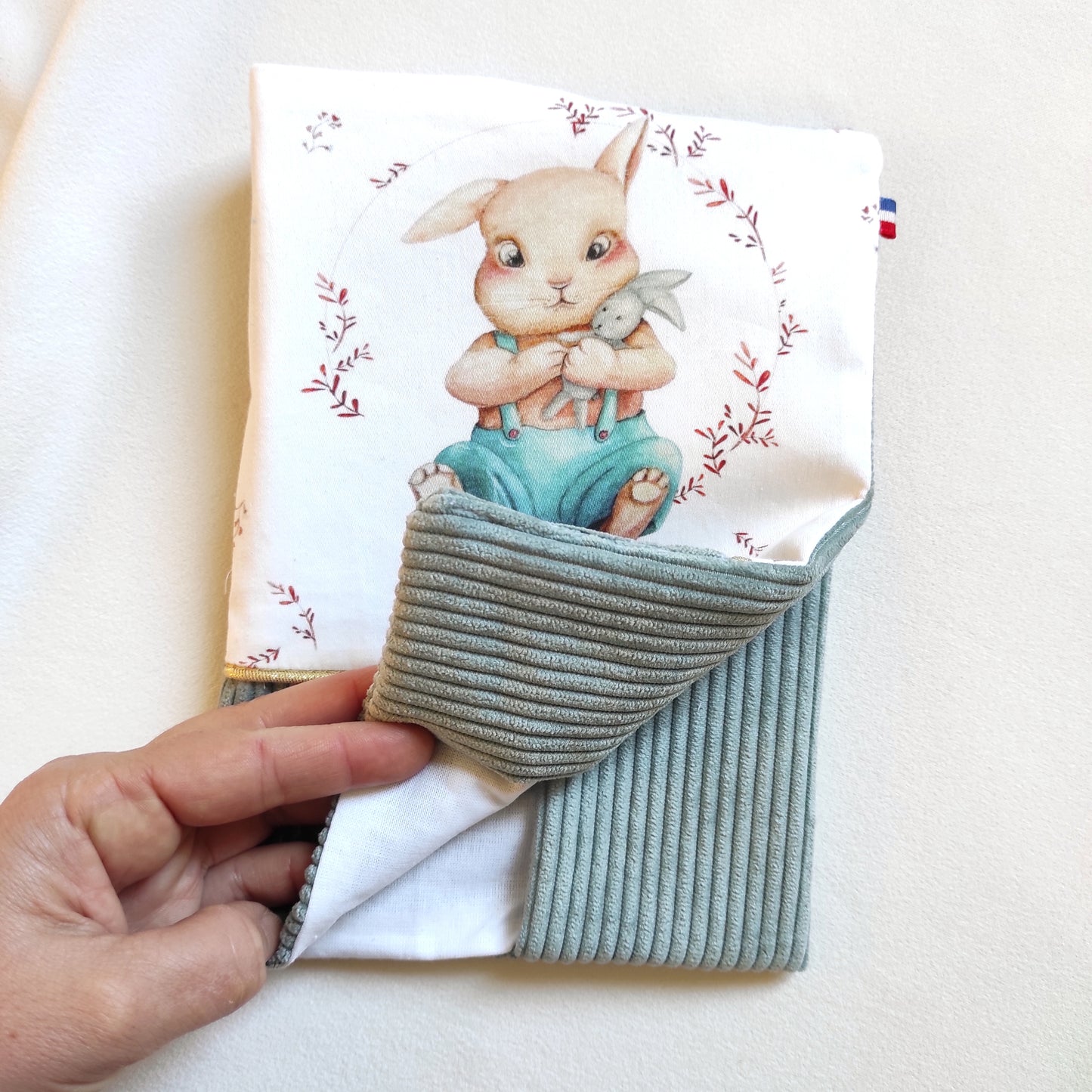Protège carnet de santé avec motif lapin et velours vert de gris, ruban doré et prénom brodé en blanc sur le velours. Intérieur du carnet en coton blanc. 