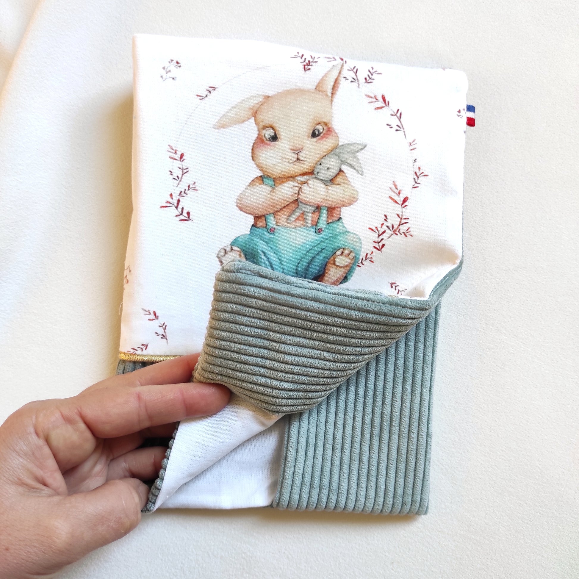 Protège carnet de santé avec motif lapin et velours vert de gris, ruban doré et prénom brodé en blanc sur le velours. Intérieur du carnet en coton blanc. 